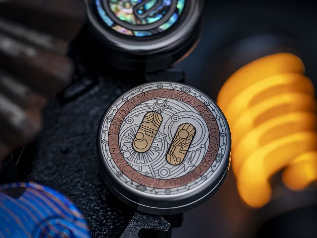 Close view of the engraved inlay pig coin, with warm-coloured rings and elongated shapes against silver-grey metal
