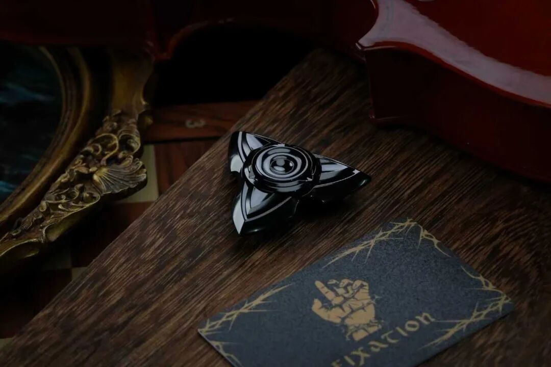The polished, heat-blackened zirconium-alloy Sword Heart on a wooden surface, with bright reflections across the blades and centre.