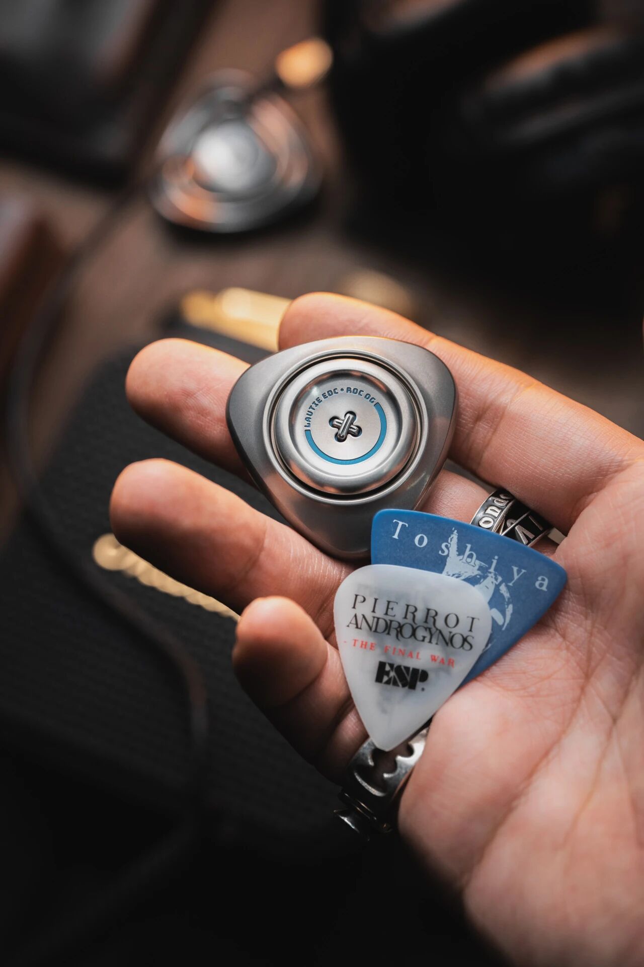 Hand-held LAUTIE ROC OG stainless steel with bright blue inner ring next to ESP guitar picks for scale reference