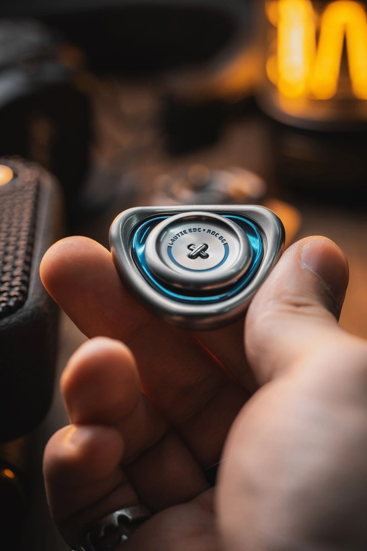 Hand-held LAUTIE ROC OG stainless steel with vivid cyan blue accent ring bokeh warm background lifestyle shot