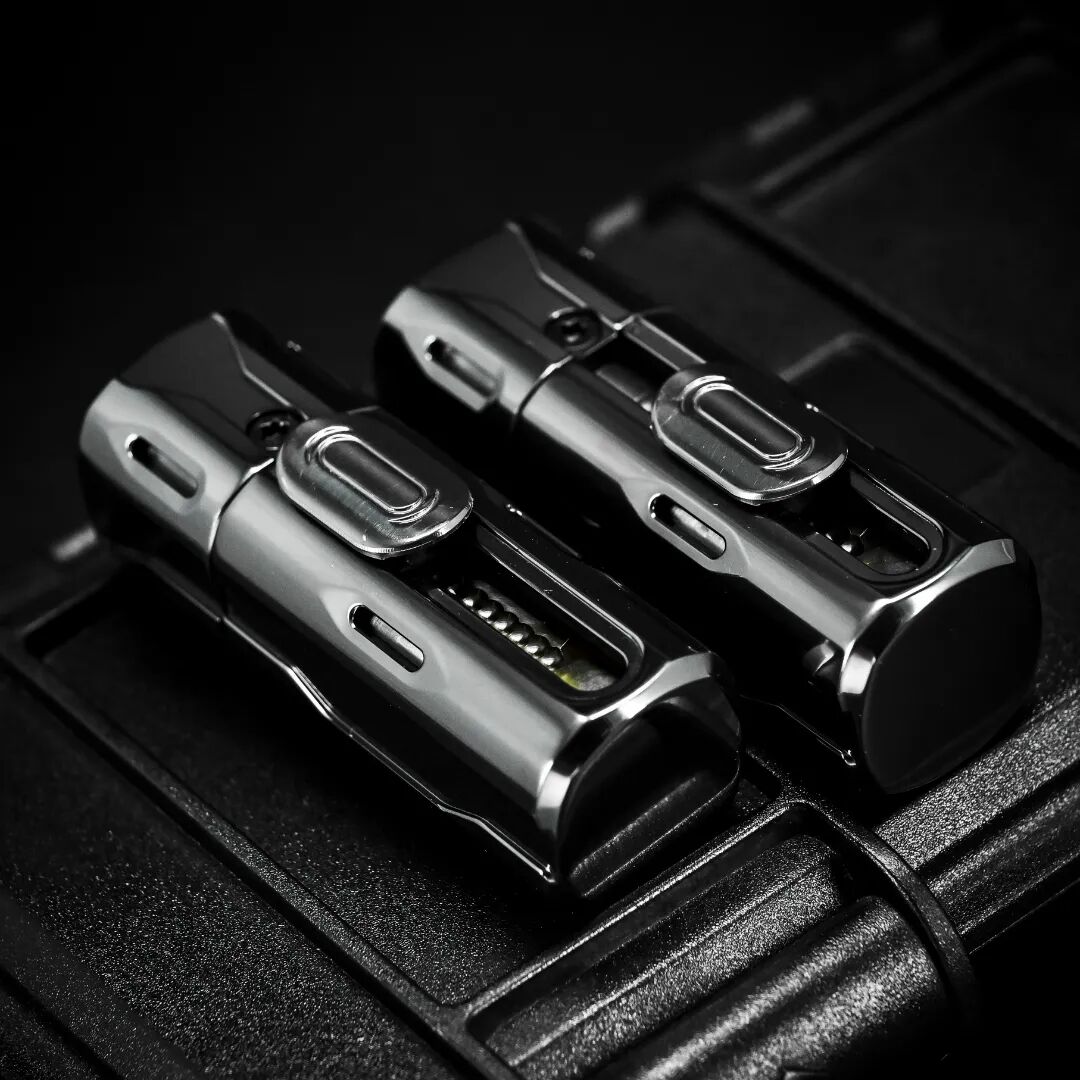 Two glossy black Phase 1.5 fidgets lie on a dark case, showing long slots and sliding controls.