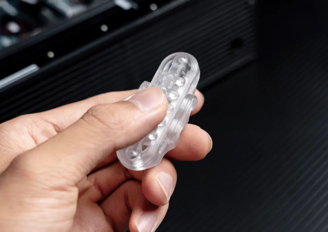 A close-up of a transparent PC Ganggu held in a hand, with edges and internal outlines visible against a dark background