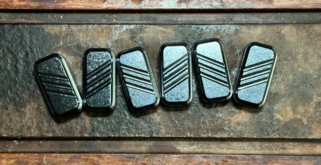 Six black crystallized zirconium Lucky Candy pieces on a metal tray, with pale texture beside diagonal grooves