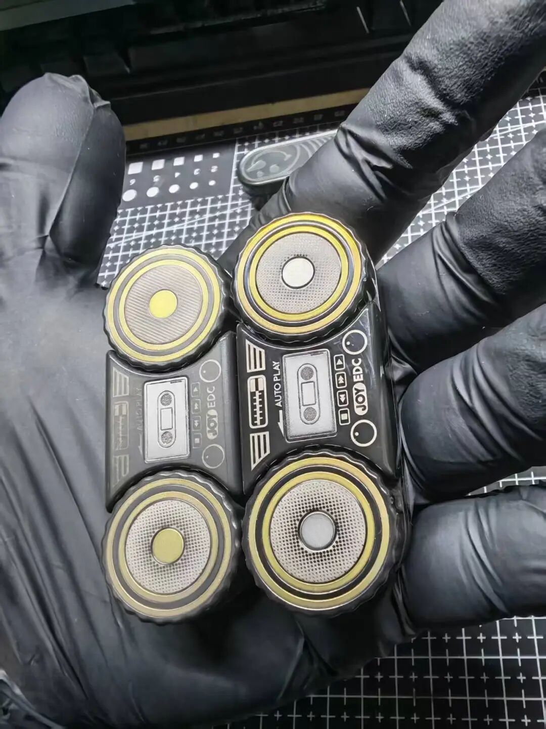 Two BGM samples rest on a gloved hand: stonewashed on the left and polished on the right. The left sample has yellow speaker-rotor centres.