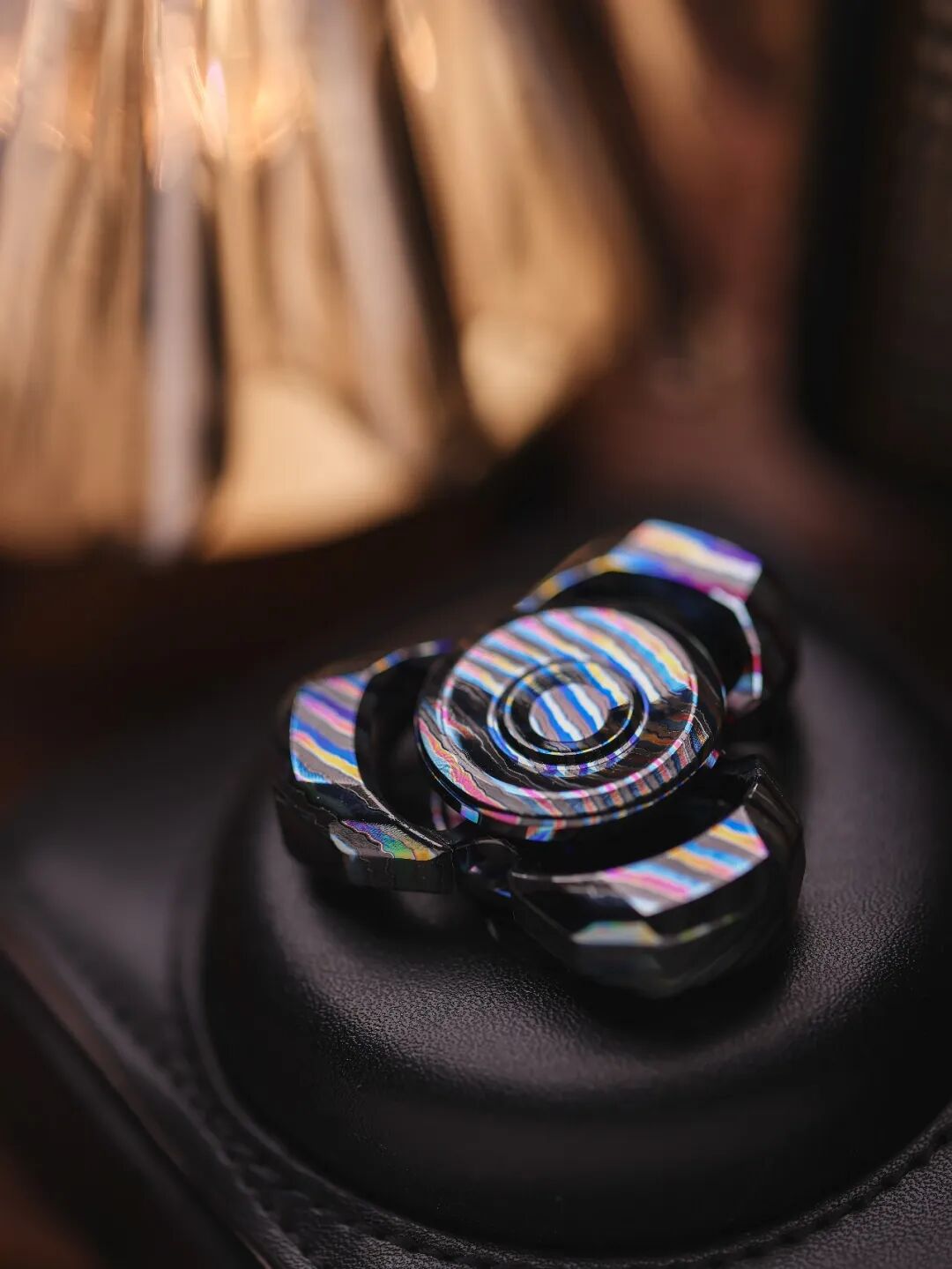A three-arm Whisper-TRI on a black cushion, with multicoloured bands across its central button and outer edges