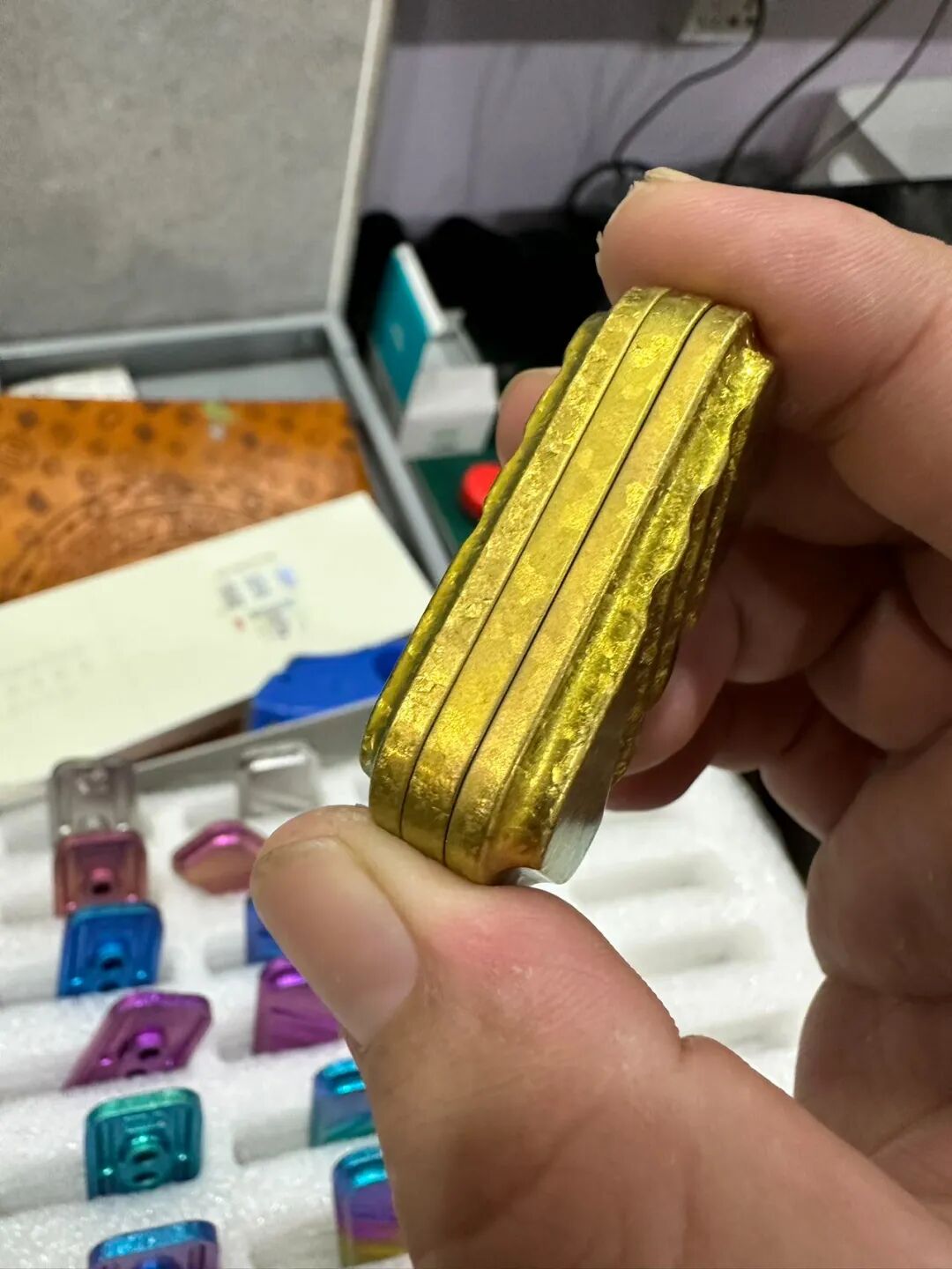 A hand holding the side of a gold-coloured crystallized zirconium Lucky Candy, showing differing sheen along its layered edges