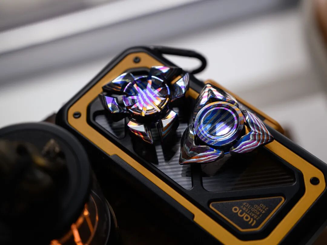 Two three-arm Zircuti spinners on a yellow-and-black mat, with different outlines and curved bands