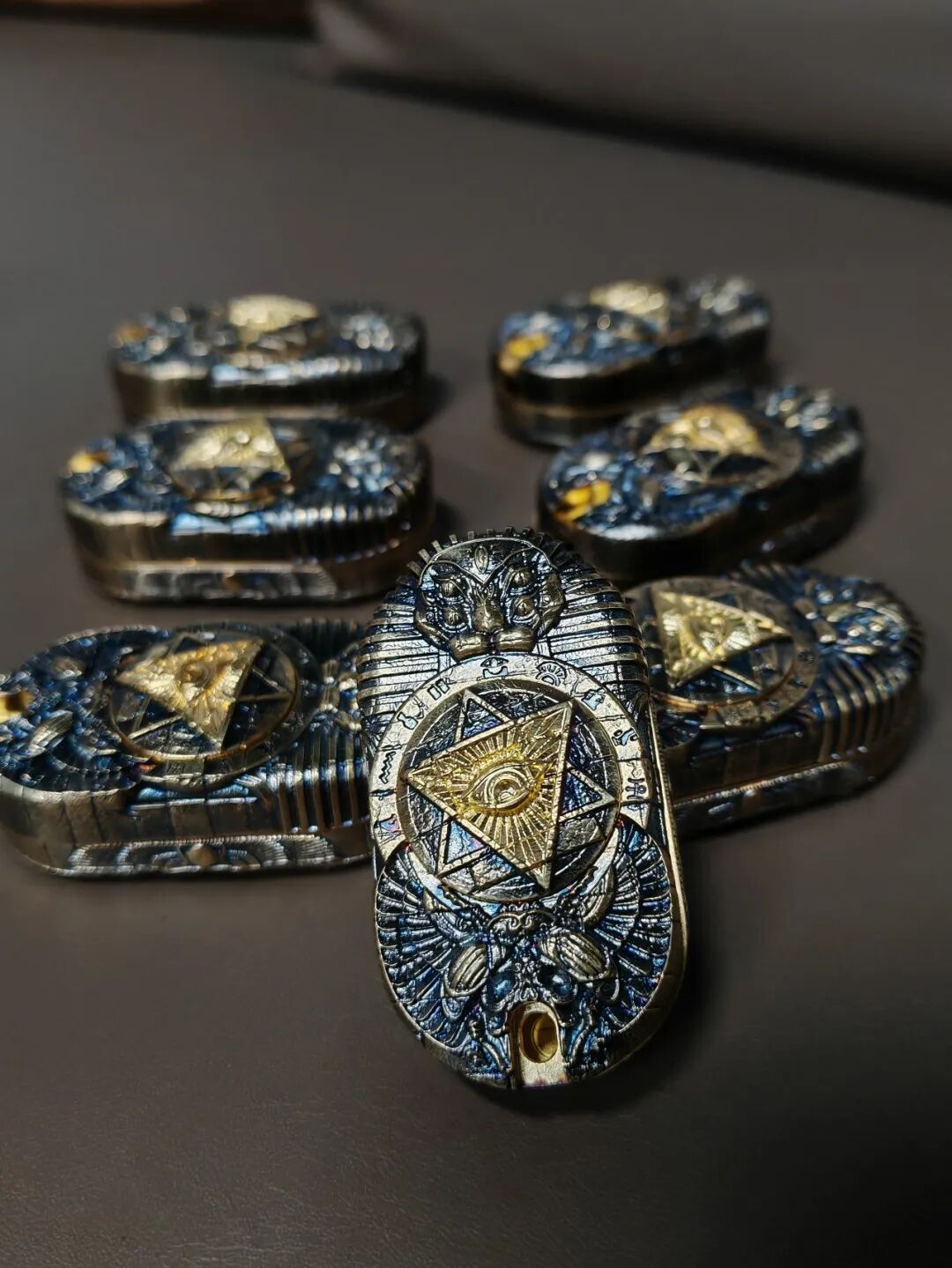 Several black-and-gold Horus Eye sliders on a desk, with one standing in front to show its eye and wing motifs.