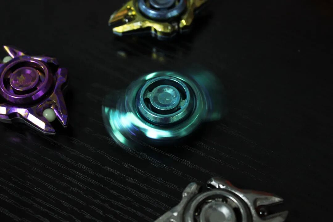 A crystallized-titanium Chang Gong spinner photographed in motion, with a green blur at the centre and other colour versions nearby.