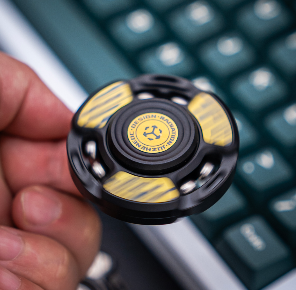 A black Fushe spinner in a hand, with yellow striped decoration on its face