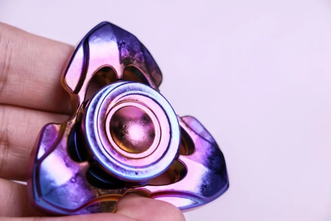 An iridescent crystallized zirconium Toothless held in a hand, with pink, purple and blue reflections on the curves and central button