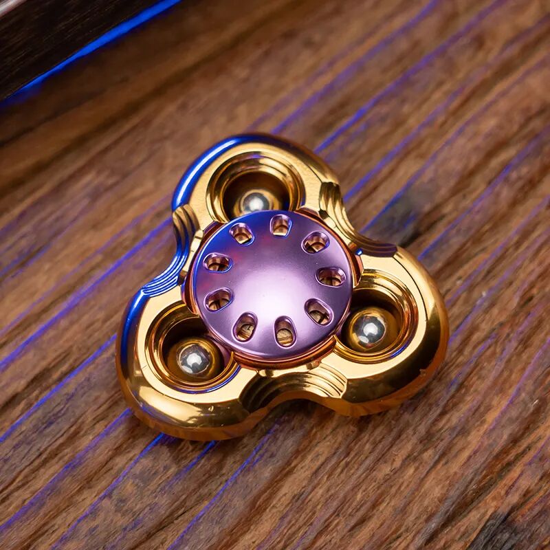 A gold three-arm Jilian with a purple button and three steel balls in outer grooves